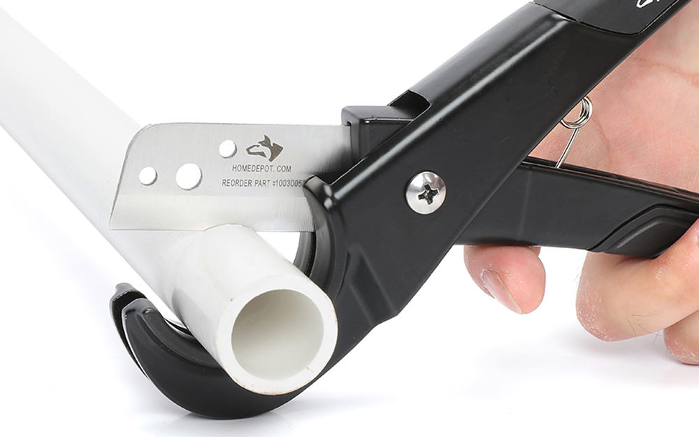 A person uses a PEX tubing cutter on a piece of PEX tubing.